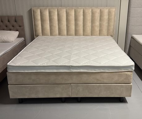 Beige tweepersoonsbed met gestikte hoofdbord en matraskern zonder beddengoed.